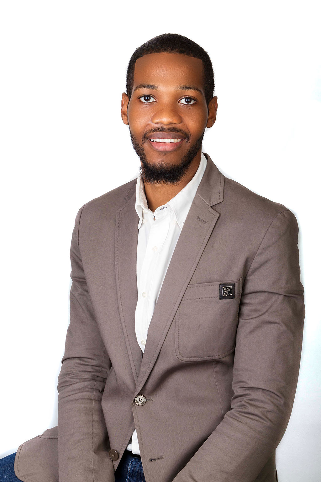 Studio headshot of a young brown-skinned male notary public named M. H. Palmer, smiling warmly, wearing a crisp white dress shirt and a tailored gray Versace blazer against a clean white background, representing Sealing Time Mobile Notaries / Notary Apostille Agents for notary public new york city services.